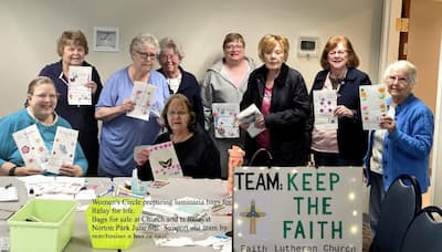 Two women sitting at a table and seven women standing holding luminaria bags they created to sell for Relay for Life.