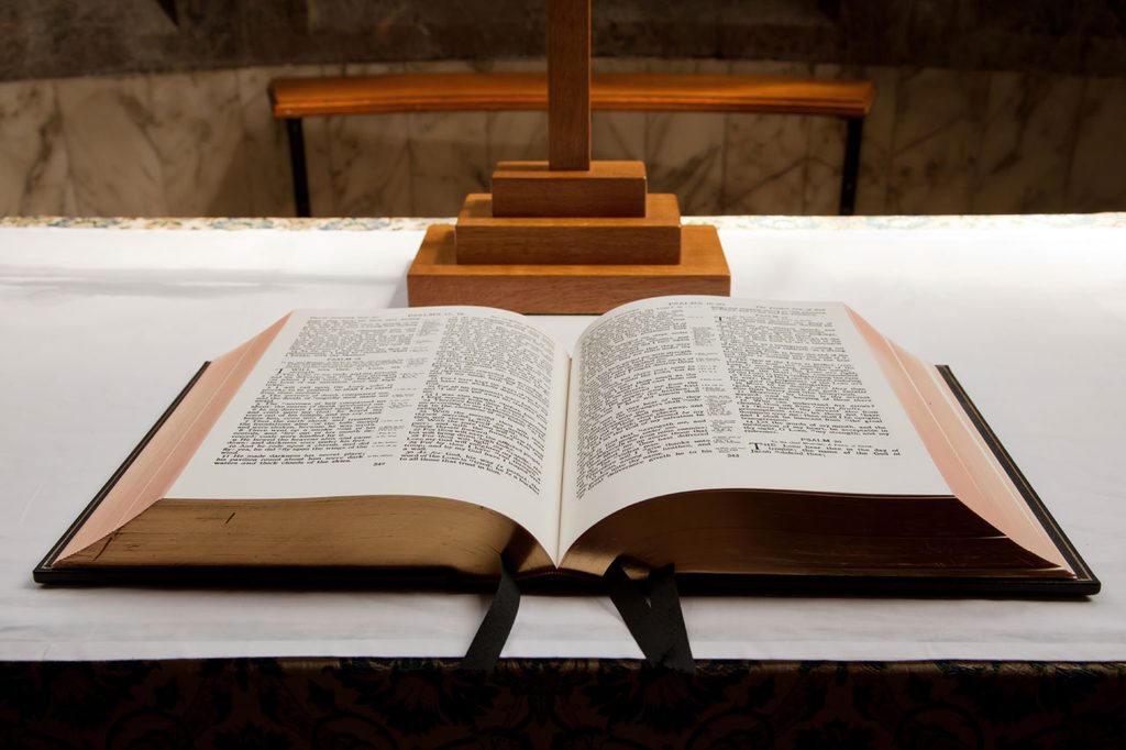 Open Bible on a white table in front of a wooden cross.