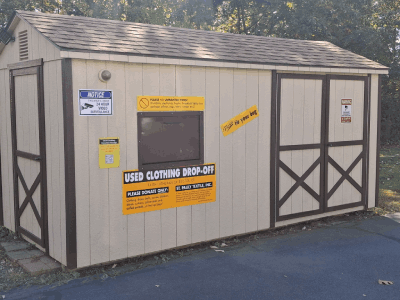 Saint Pauly Shed is light brown with dark brown accents on the doors. Signs on the shed show where to drop off clothing.